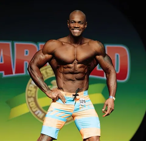 Antony Bessala smiling on stage in front of an Arnold Classic backdrop, number 529