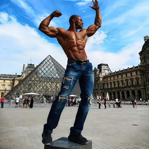 Antony Bessala posing on a plinth in front of the Louvre pyramid in Paris