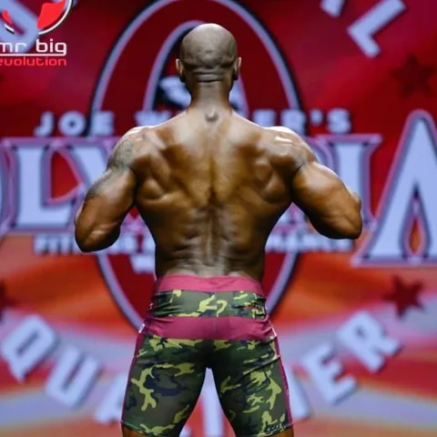 Antony Bessala seen from behind in front of the Mr Big Evolution Olympia qualifier backdrop