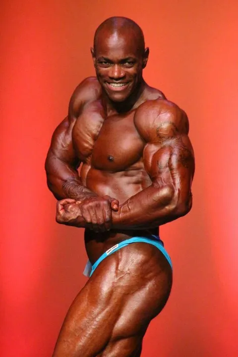 Antony Bessala on the Musclemania Pro stage: most muscular pose in blue trunks against an orange backdrop