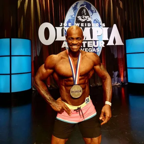 Antony Bessala with a medal in front of the Joe Weider's Olympia Amateur Las Vegas sign